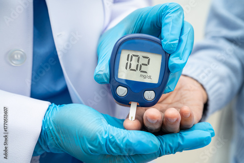 Asian doctor using digital glucose meter for check sample blood sugar level to treatment diabetes.