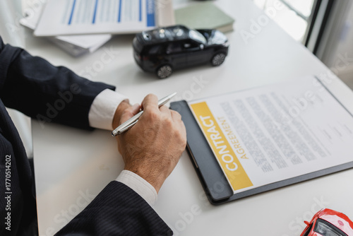 A businessman in a suit is calculating loan details, reviewing financial documents, and holding car keys near a calculator and toy car models, representing auto loan and finance services.