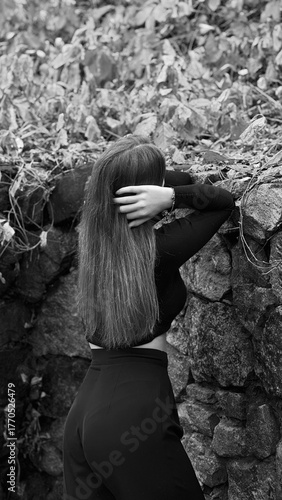 A woman in a black crop top and wide-leg pants stands by a stone wall on the steps in a park. She has her head thrown back and is relaxedly breathing in the fresh air, enjoying a moment of peace.