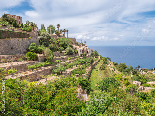Banyalbufar, Mallorca. picturesque coastal village with terraced gardens and historic buildings sits on a hillside, overlooking the sea under a partly cloudy sky, Majorca