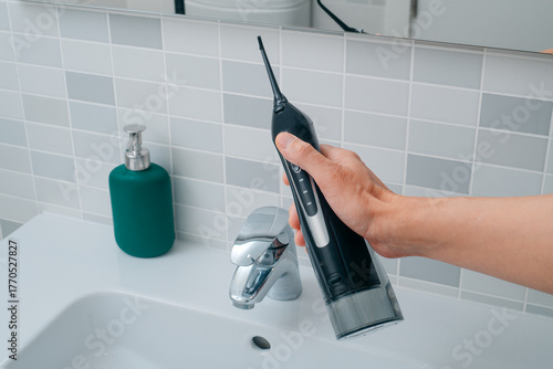 a man holding an oral irrigator in the bathroom