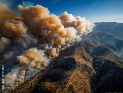 Wide aerial view of a massive forest fire releasing smoke over dry hills and valleys during heatwave