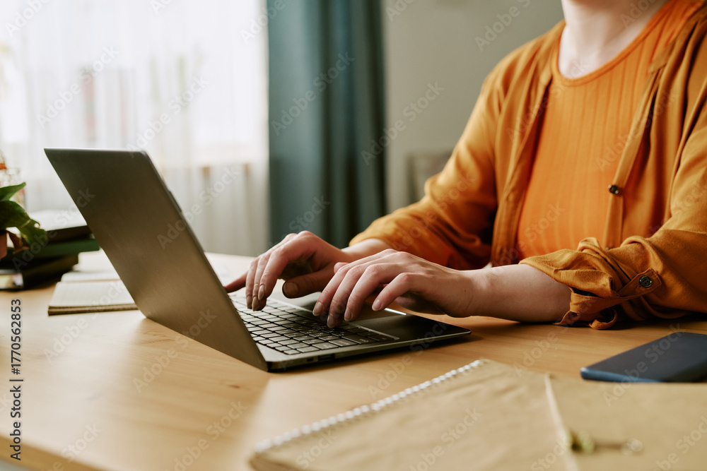 Fototapeta premium Caucasian young adult woman sitting at desk typing on laptop, hands and upper body visible, showing partial hair loss on scalp, concept of alopecia and remote work