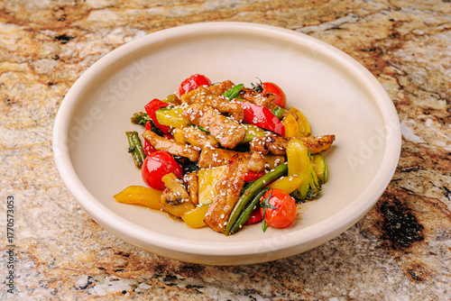 Colorful stir-fried vegetables with chicken served in a bowl on a stone surface