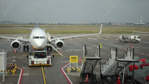 Static plane, Plane tarmac, Ground loading. Cloudy weather surrounds parked airplane at airport gate with ground support and equipment.