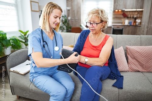 Nurse checks blood pressure of senior patient in cozy living room setting