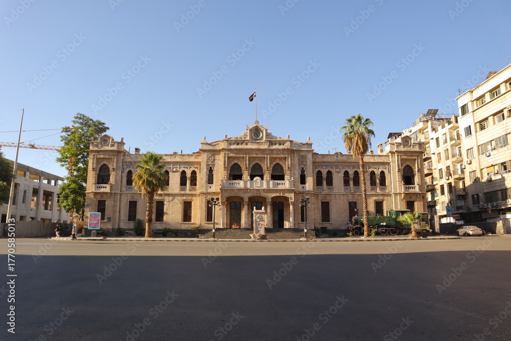 Obraz premium Damascus, Syria 08.08.2025 Historic Hijaz Railway station with Islamic architectural design and the new Syrian revolution flag waving above. Iconic Middle Eastern travel and cultural heritage landmark