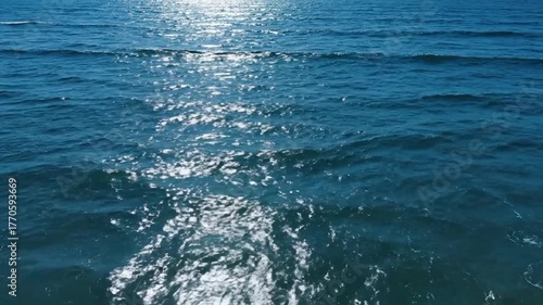 Aerial view of sparkling blue ocean waves under sunlight, with white foam