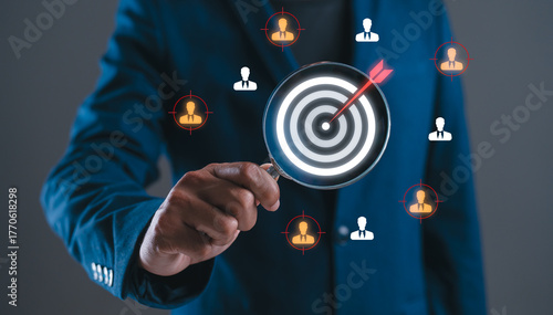 A person in a suit holds a magnifying glass over a target, symbolizing focus on identifying key individuals in a professional context.