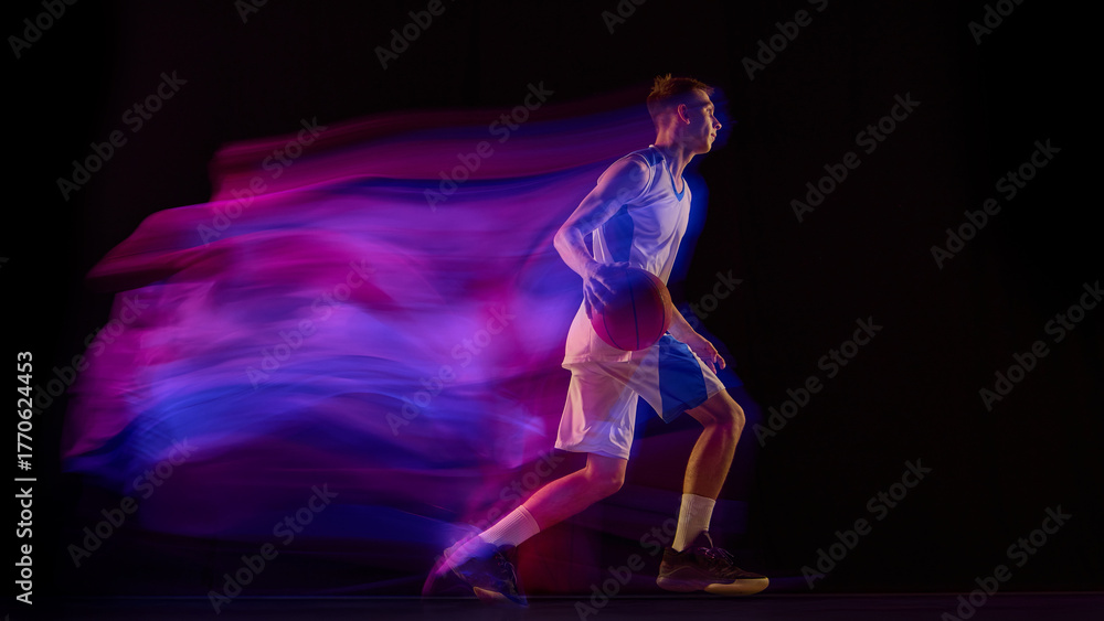 Fototapeta premium Basketball player dribbling ball in blue and purple motion light on dark background. Concept of brand identity, sport marketing, energy training, and expressive movement style.