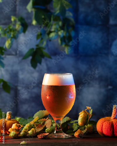 glass of light beer on a wooden table with green hops and small pumpkins