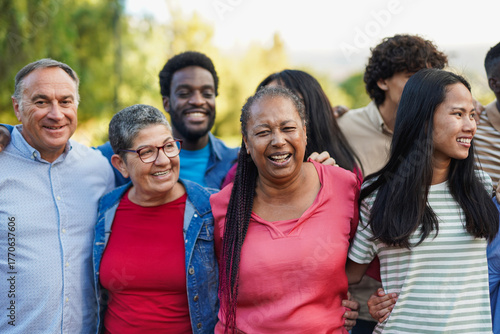 Crowd of multi generational people hugging each other in front of camera at city park - Multiracial friends, community and social inclusion concept