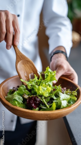Close Up Shot of a Person Tossing Mixed Greens with Wooden Tongs. Arranging a Healthy Salad Plate in a Contemporary Kitchen. Clean Food and Mindful Eating Concept. 