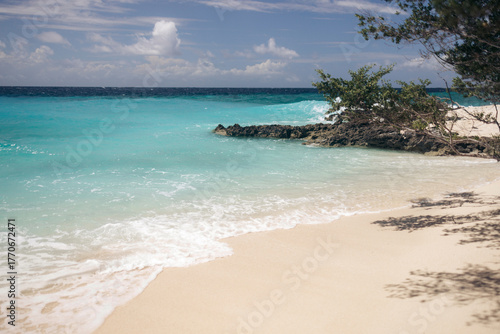 Serene beach with turquoise waves gently lapping on white sand under a partly cloudy sky. Pulau Nailaka or Nailaka Island, Banda, Central Maluku, Indonesia