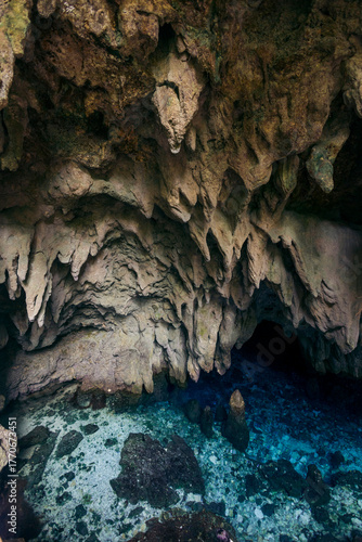 Intricate limestone cave interior with stalactites and a clear blue water pool at its base. Air Goa Hawang or Hawang water cave in Kei Kecil, Southeast Maluku, Indonesia
