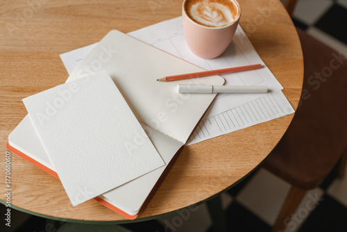 Close-up overhead view of a blank paper card, to do list, an open notebook, pen and pencil, cup of cappuccino on a table.