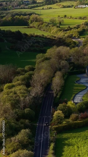 This is a video of the Irish countryside in West Cork taken from the air. On a sunny day in Ireland, you can see green fields, trees, houses and a small winding road.