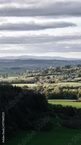 Rolling hills under a cloudy sky. Lush green fields stretch to the horizon.