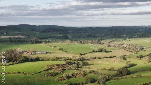 An elevated long view reveals lush green fields and picturesque farmland in West Cork, Ireland. The early morning light illuminates the rolling hills landscape.