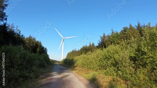 Wind turbine spinning on a clear day. Wind farm in a lush green forest. Eco-friendly energy production with turbines.