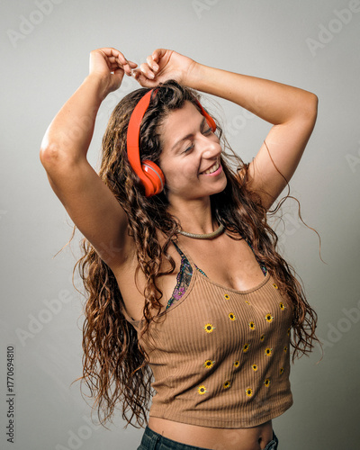 Joyful young woman enjoying music while dancing with vibrant headphones on a clean background