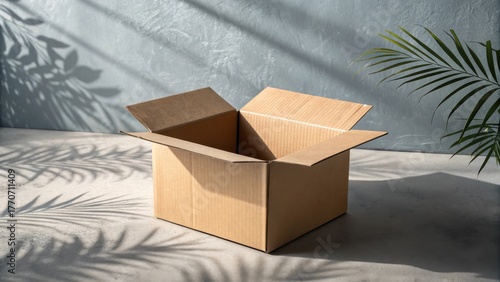 An open empty cardboard box on the floor with tropical plant shadows and natural sunlight, ideal for packaging or shipping concepts.