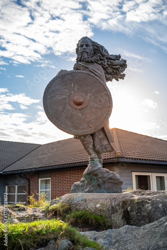 King Harald, Fairhair statue, bearded warrior holding a shield stands in front of a house with a cloudy sky, sunbeam, vertical shot, Haugesund, Norway