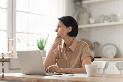Tableau sur toile Pensive mature female hesitating over business decision by notebook screen