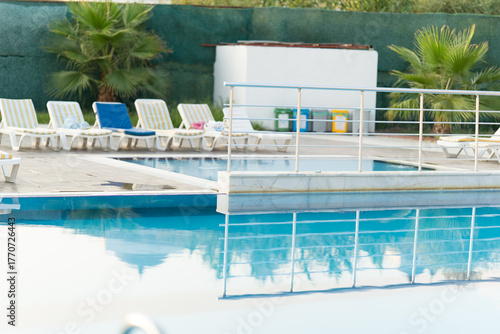 Tranquil swimming pool area featuring lounge chairs, palm trees, and clear blue water reflecting the serene environment, perfect for relaxation and leisure activities