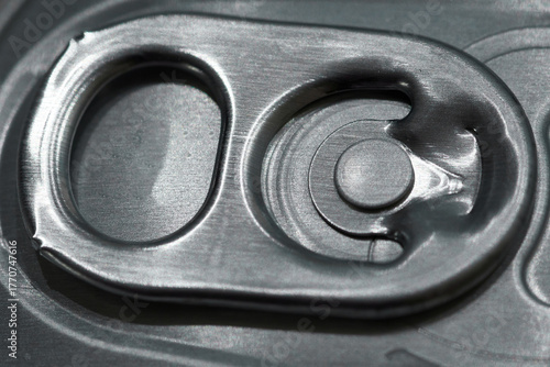 Close-up macro shot of a soda can pull tab showing the metallic surface and texture. Industrial and geometric design, useful for themes related to beverages, recycling, packaging, and minimalism.