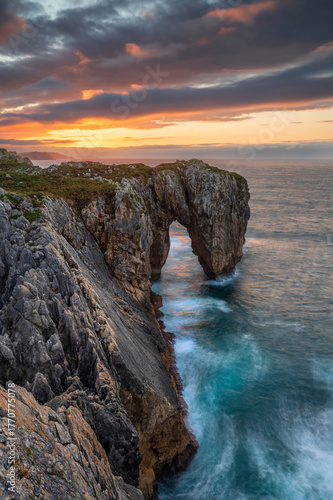 Natural arch at Punta Pena Flecha at sunset in Acantilados del Infierno near Ribadesella, Asturias, Spain. Wonder nature landscape with vivid sunset colors.