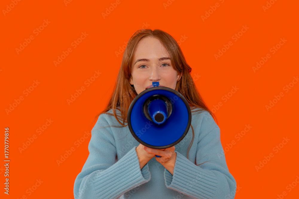 Obraz premium Young woman holding a blue megaphone on a bright orange background to make an announcement or rally support