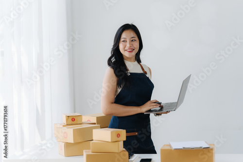 E-Commerce Startup Success: A determined entrepreneur stands amidst parcels, confidently operating a laptop, poised to grow her online business.