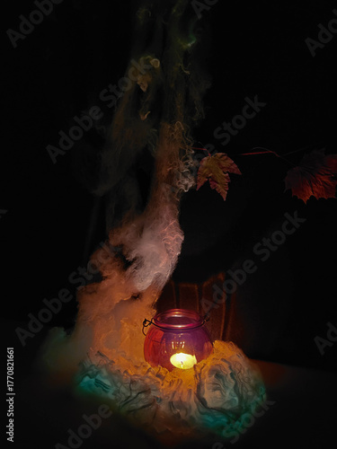 A burning candle in an orange pumpkin-shaped lamp with a white glowing spider web.