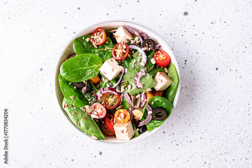 Fresh vegan salad with baby spinack leaves, tofu, cherry tomatoes, onion and seeds in ceramic bowl on white stone table top view. Healthy diet food concept.