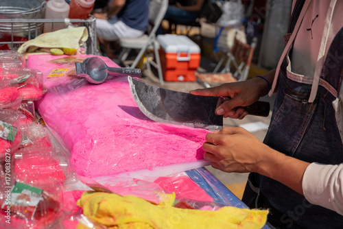 Fotografia Turrón Candy, Close up of a man's hands slicing a block of bright pink artisanal nougat with a long knife