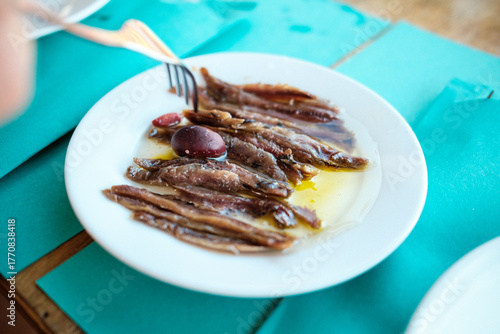 Eingelegte Anchovis (Sardellen) in Öl mit Olive am Tisch, Gabel greift hin