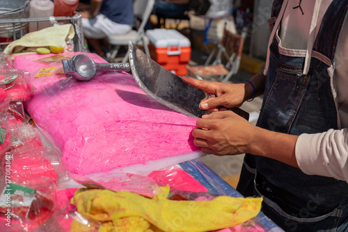 Turrón Candy, Close up of a man's hands slicing a block of bright pink artisanal nougat with a long knife. The confection is being sold at a street vendor stand. Turron