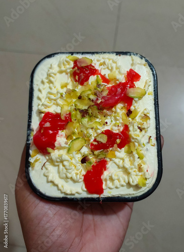 Hand holding sweet dish topped with dry fruit and cherry, food background, dessert photography, dairy ice-cream