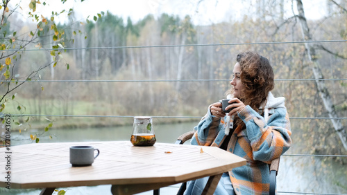 A sweet woman with curly hair drinks tea and relaxes on the terrace of her house on an autumn day. Health care, sincerity, a sense of balance and calm.