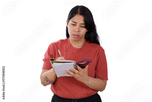 Woman wearing a red shirt on a white background, writing in a notebook, while she looks at her cell phone