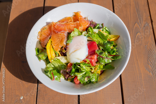 Fresh salad bowl with smoked salmon and poached egg served outdoors