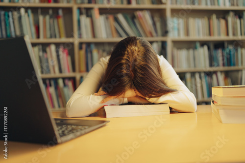 Tired student asleep on books in library, academic burnout