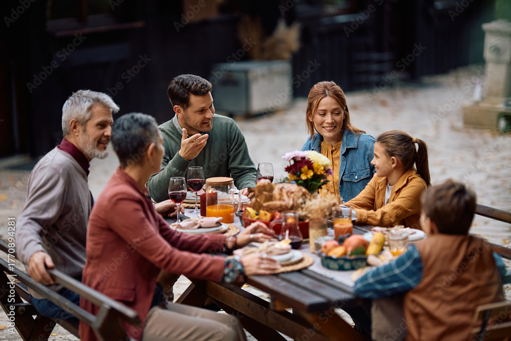 Obraz premium Happy multi-generation family talking while having Thanksgiving meal on patio.