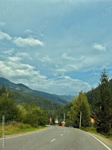 Curving asphalt road leading through forested mountains on a sunny day. Beautiful travel scenery with nature, trees, and distant hills.