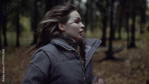 Frightened woman running through dark forest and looking back in fear