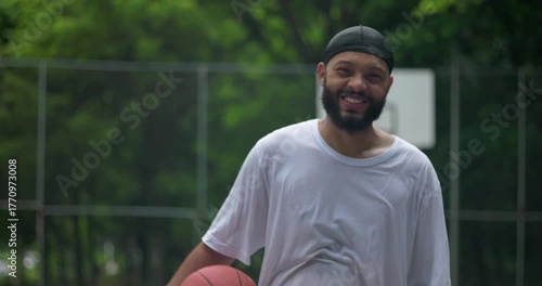 African American man smiling and holding basketball on outdoor court, moment of joy and relaxation after game symbolizing friendship, confidence, and urban community spirit