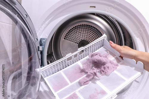 close up female hand taking lint out from dirty air filter of dryer machine after drying. cleaning Dirty filter. hair, wool from filter in hand. Front Load Tumble Laundry electric Dryer Machine. 