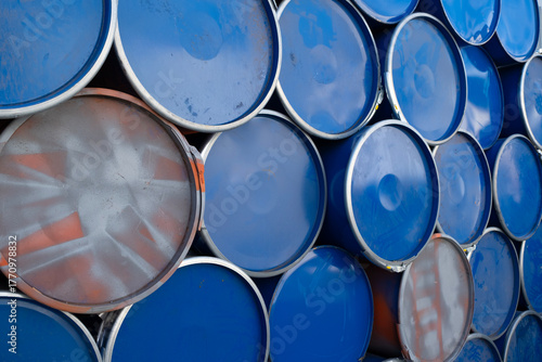 Blue and silver metal barrels arranged in rows. Stack of used metal barrels in industrial area. Stacked blue and gray metal barrels in storage yard. Industrial storage of recycled metal drums.