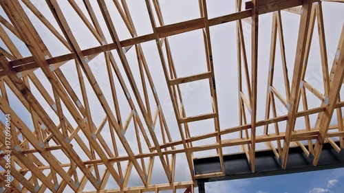 Wooden beams form complex structure for building roof as workers prepare for construction.